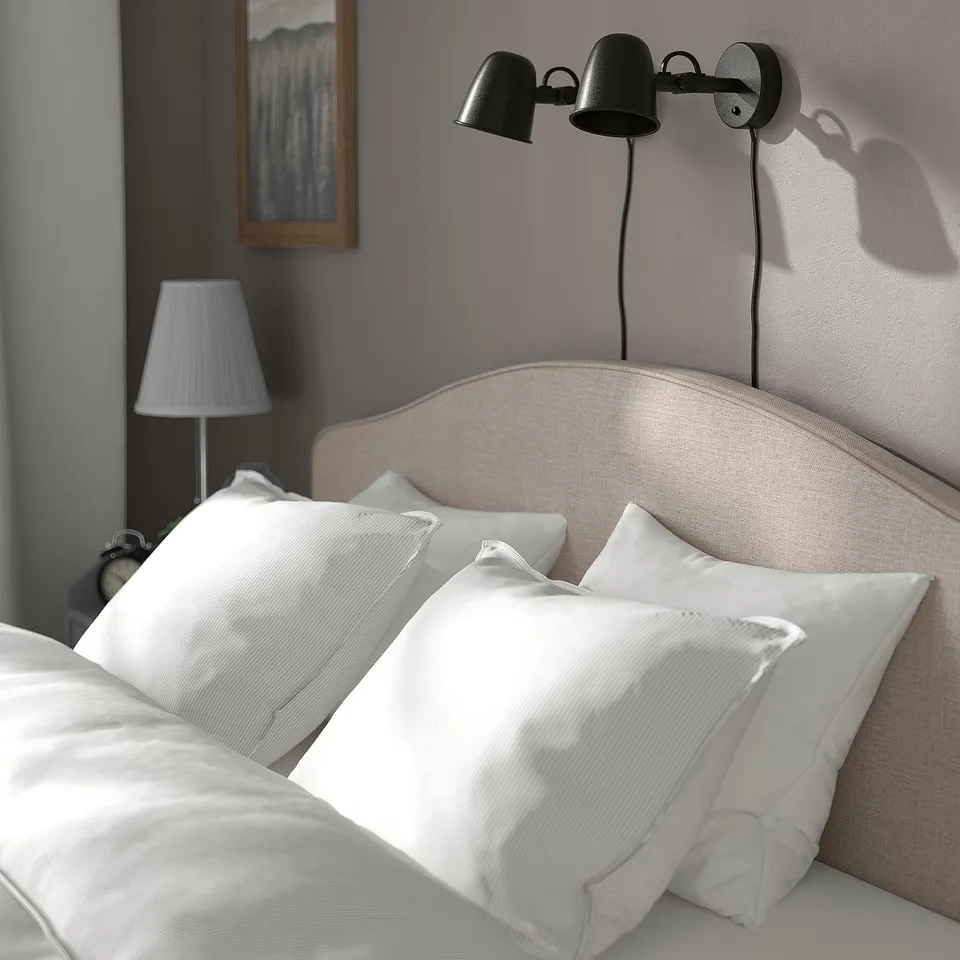 Modern bed with soft headboard, wall lamps, white pillows, and grey fabric headboard panel.