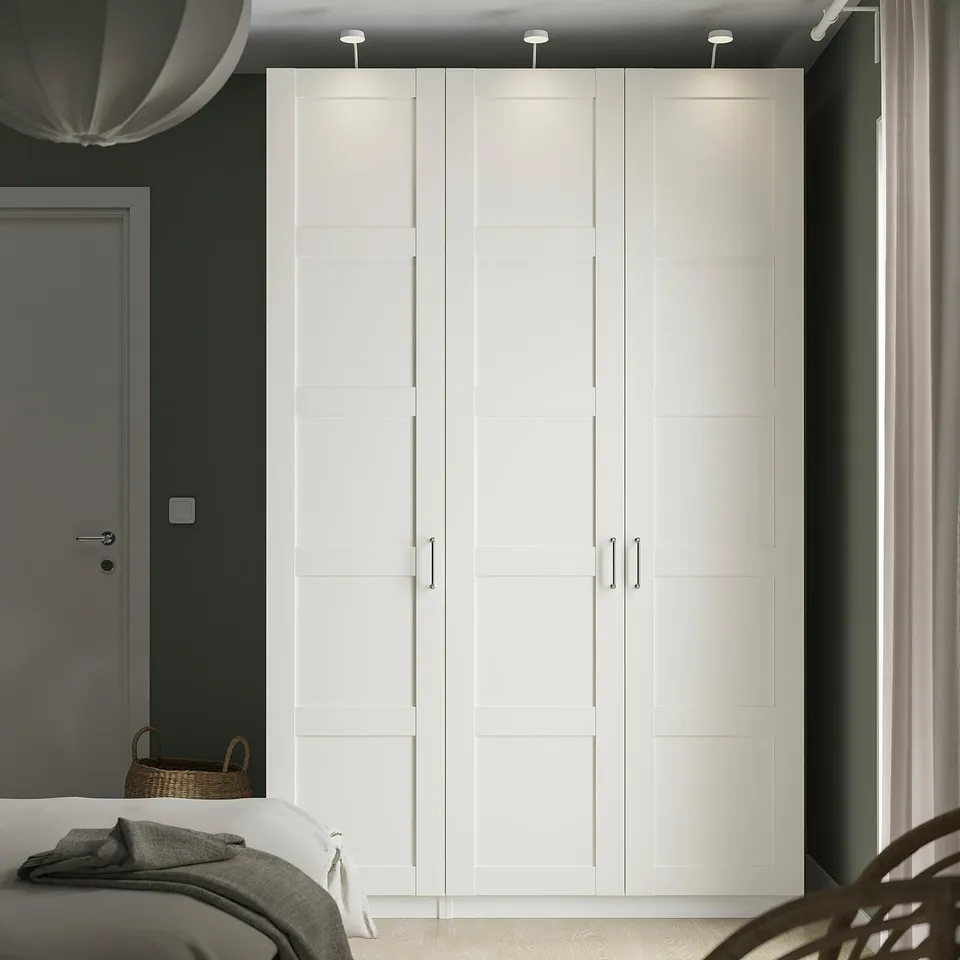 Large white PAX wardrobe with sleek design dominates room, tall and wide, fits neatly beside door.