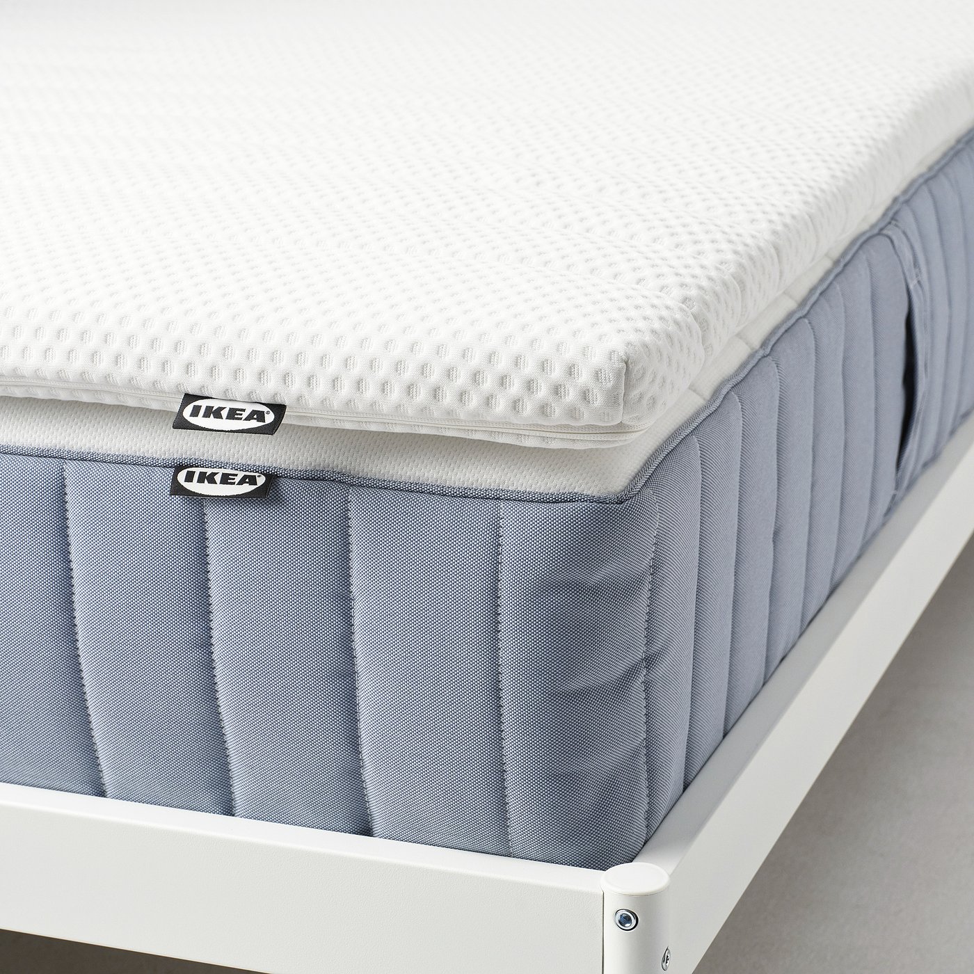 An IKEA NISSEHOLM mattress pad displayed, featuring a grey high-resilience foam base and a white, textured top layer for firmer feel support.