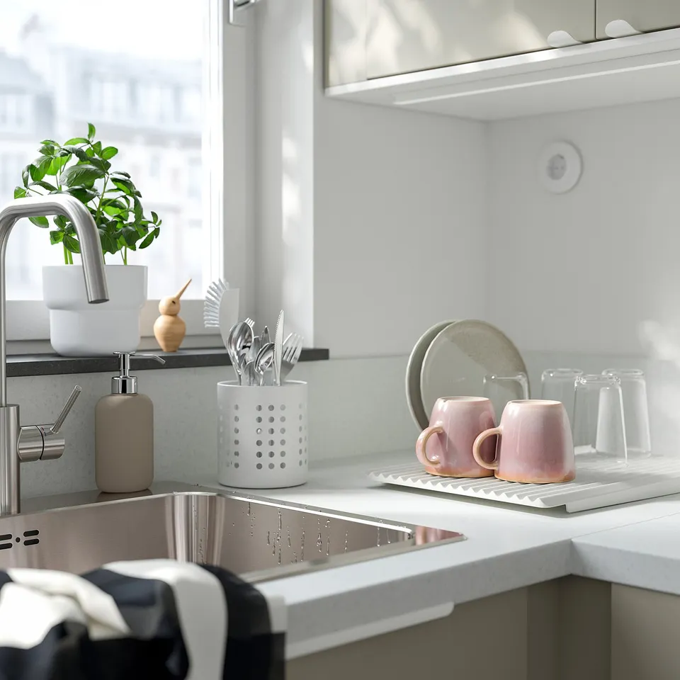 Modern kitchen sink with stainless steel tap, utensil holder, two pink mugs, a plant, and a soap dispenser.