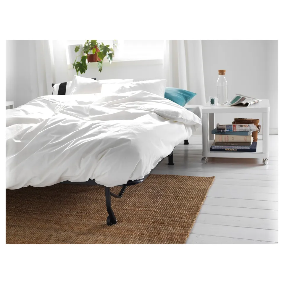 A white wooden bedside table on wheels, holding a water bottle, a blue pillow, and some books.