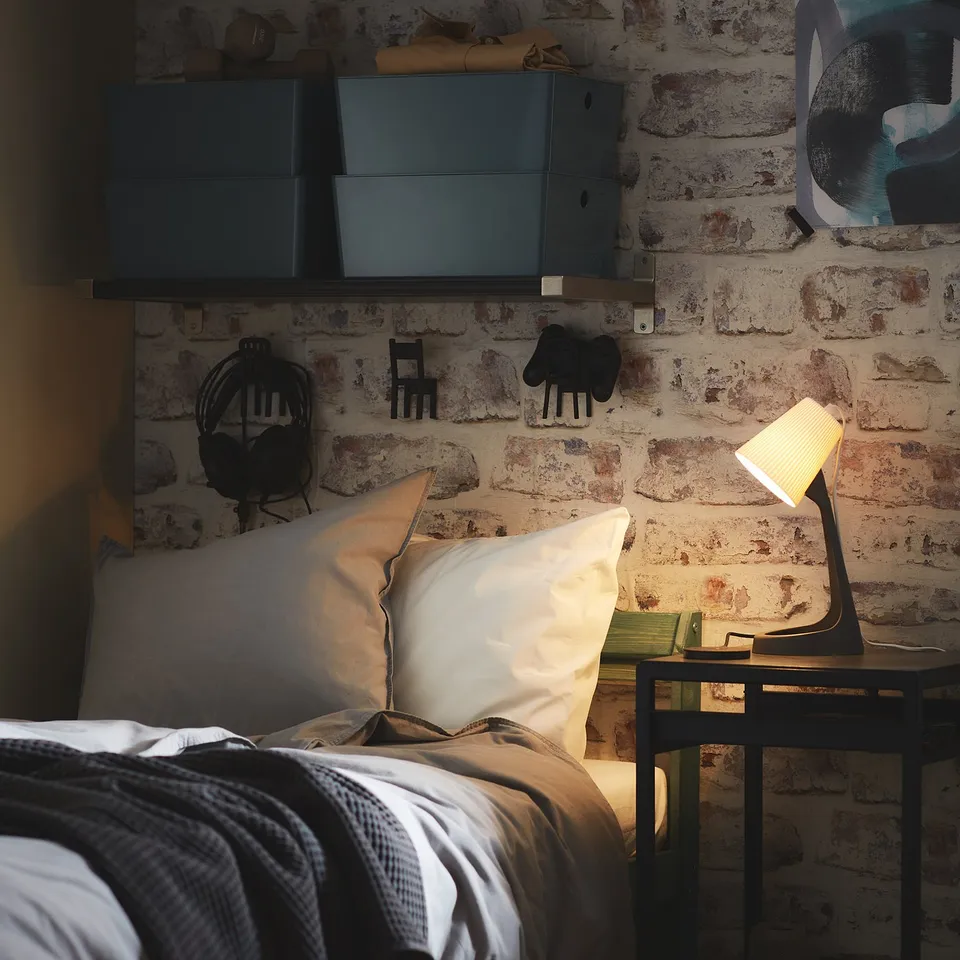 Cosy bedroom with brick walls, white pillows on bed, modern lamp on bedside table.