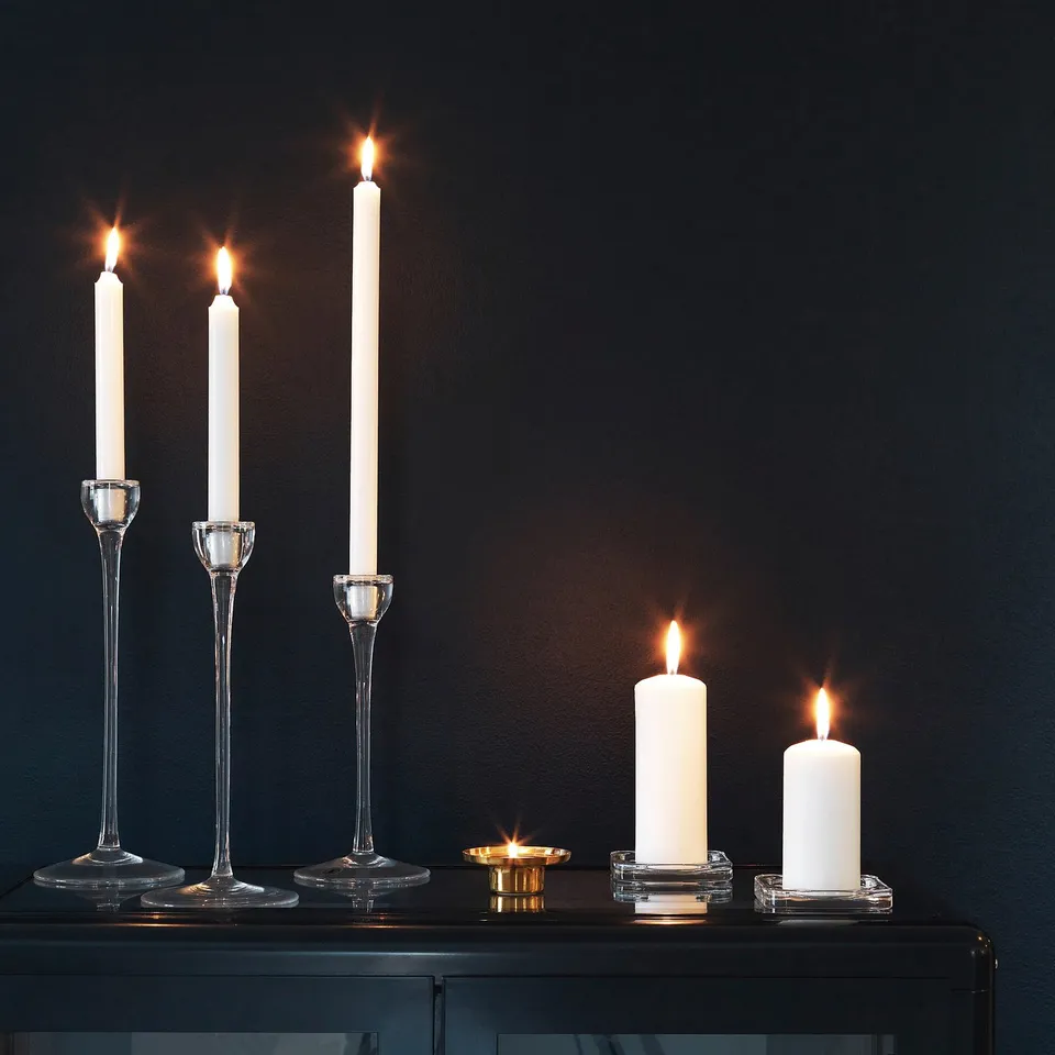 Six lit white candles in clear glass holders on a dark surface.