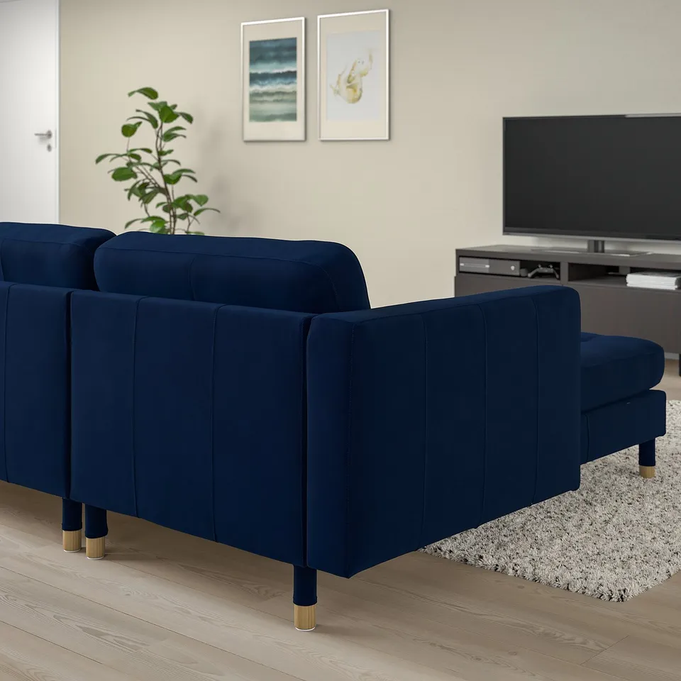 Modern room with large blue velvet sofa, wooden floors, plant, tv, and wall art. Sofa fits well in spacious living area.