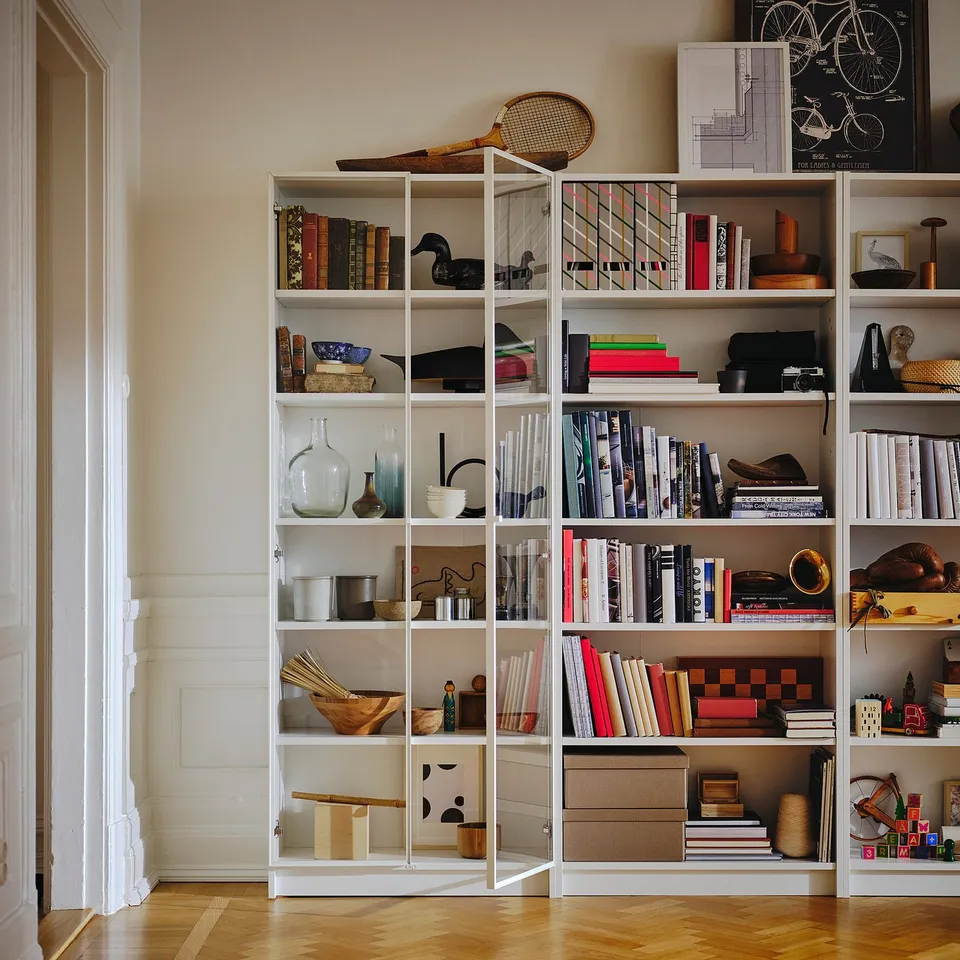 White BILLY bookcase filled with books, vases, and decor on wooden floor.