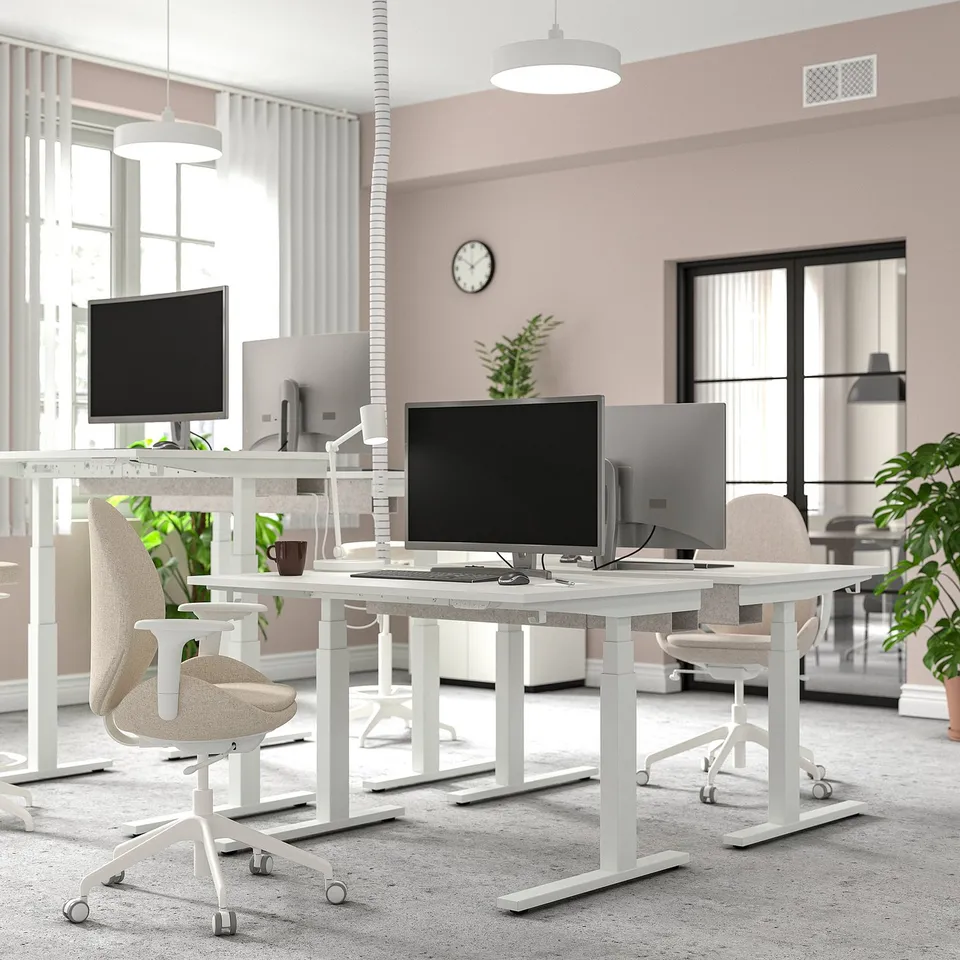 Modern office with MITTZON sit-stand desks, dual monitors, ergonomic chairs, large windows, and pendant lamps. Pink walls, ample legroom.