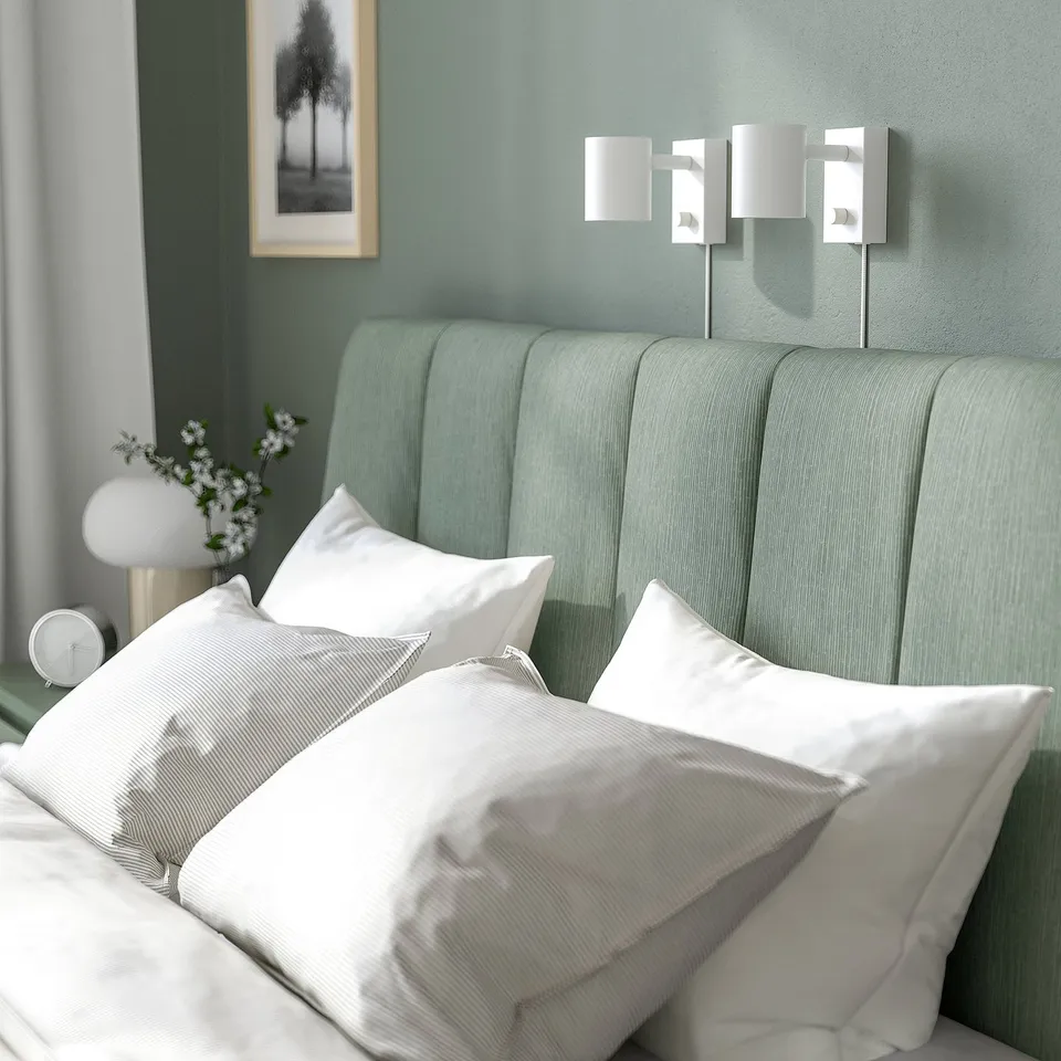 Modern bed with padded headboard, clean lines, and adjustable bed sides. White pillows and linens on green bed, wall-mounted lights nearby.