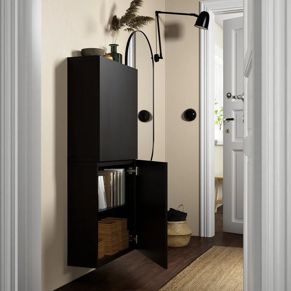 Black wall-mounted cabinet with one door open, displaying files and wooden boxes. Shown next to a wicker basket and a black wall lamp.