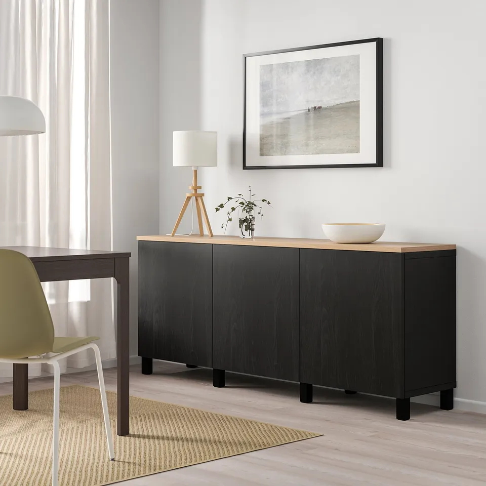 Black BESTÅ sideboard with light wood top. Minimalist decor with photo, lamp, and bowl.