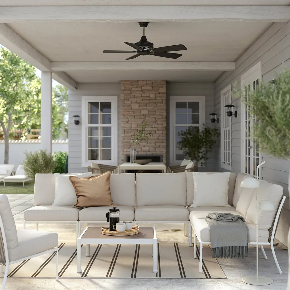 Modern outdoor patio with cream-colored sectional sofa, coffee table, and striped rug under a black ceiling fan.