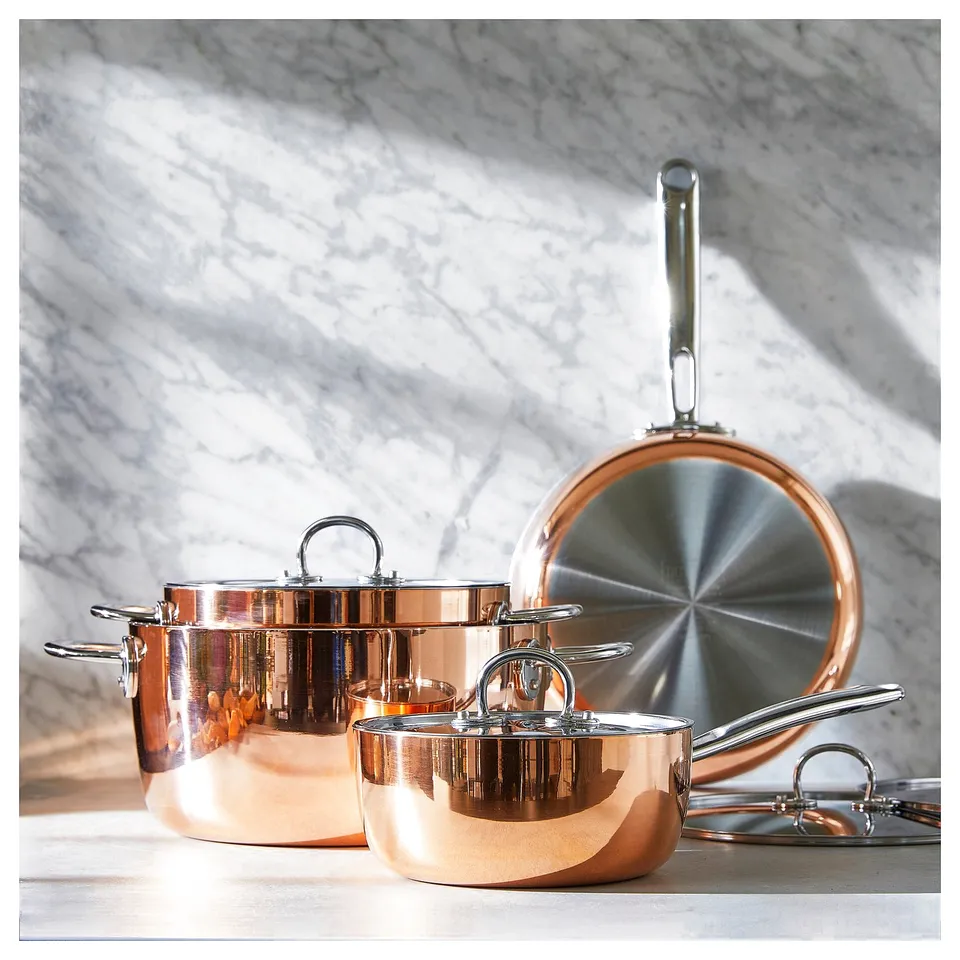 FINMAT copper cookware set, gleaming copper pots with stainless steel rims and handles, reflective interiors, displayed on marble surface.