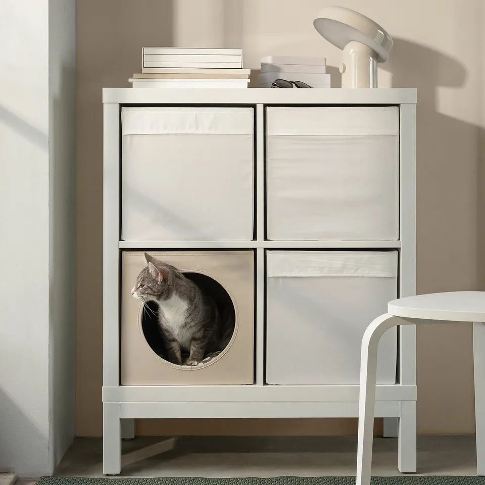 White UTSÅDD cat house in kallax shelf with cat, books, lamp, stool.