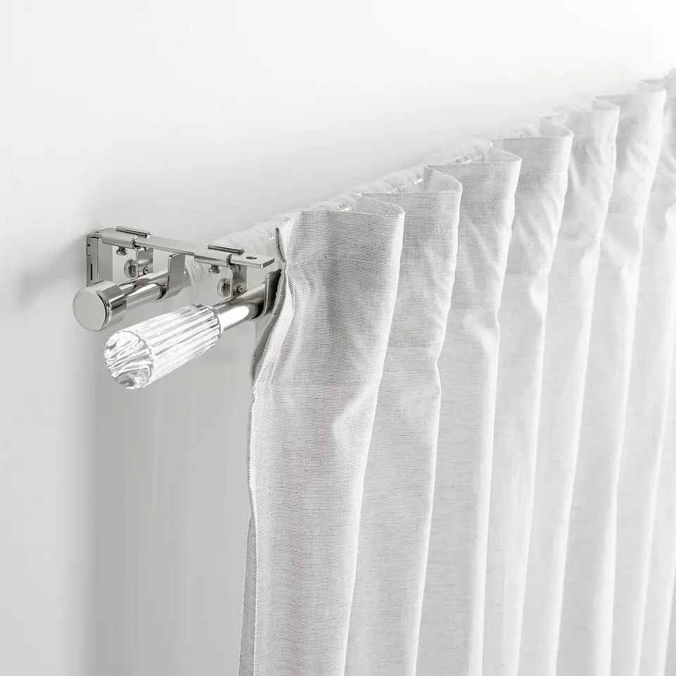 Close-up of chrome curtain rod bracket holding white curtains, showcasing part of soldvärm set.