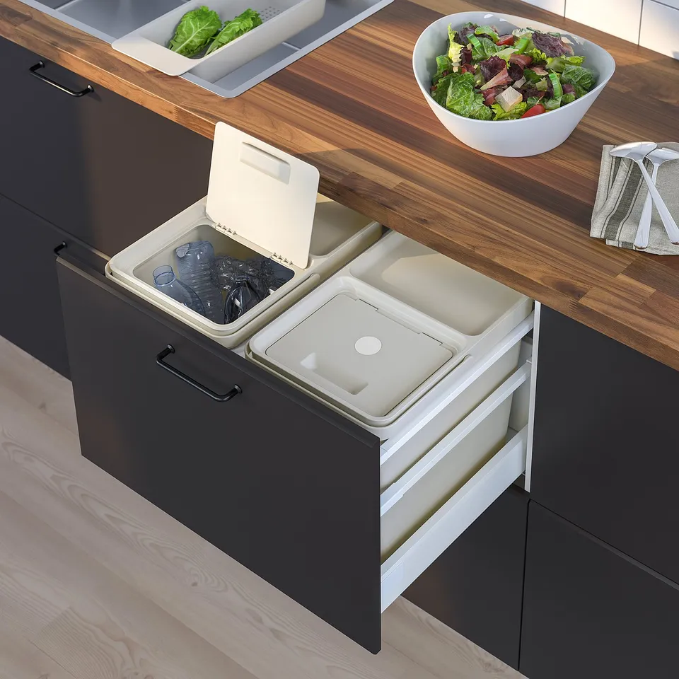An open black HÅLLBAR waste sorting drawer with two plastic white bins: one containing empty plastic bottles.