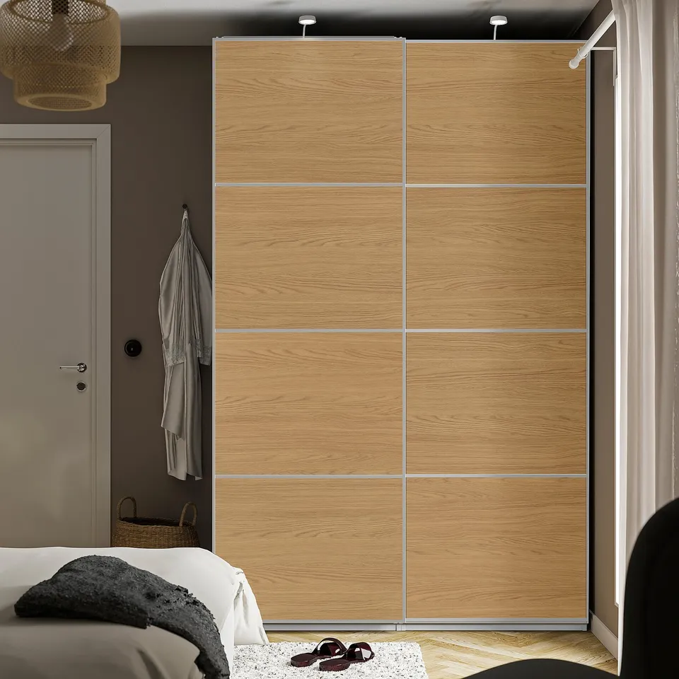 Mehman light oak wooden sliding doors, part of a pax wardrobe, beside a bed, taller than the bed.