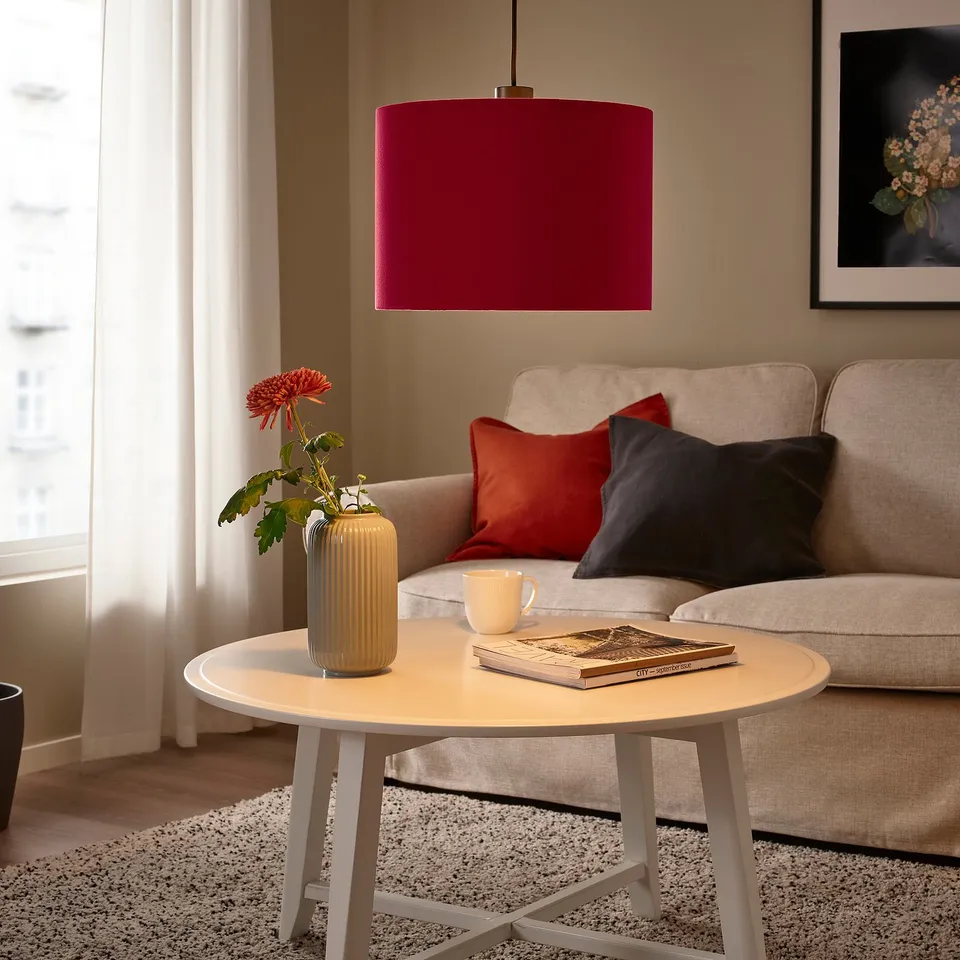 Stylish living room with beige sofa, red pillows, large SUNNEBY lamp, coffee table, books, and flowers.