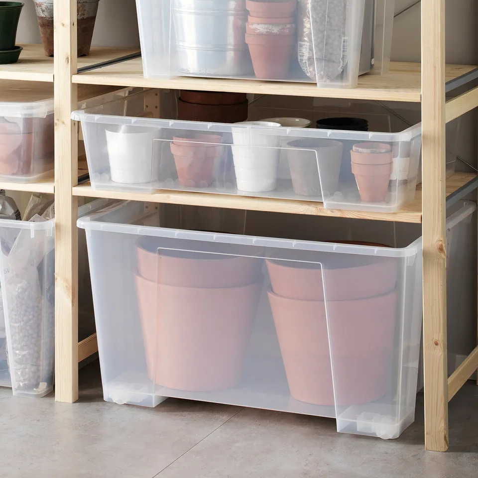 Clear SAMLA boxes store flower pots on a wooden shelf, some with wheels, stacked vertically and horizontally.
