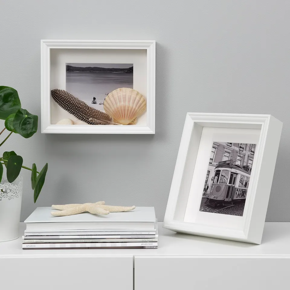White frames VÄSTANHED display photos beside books and plant.