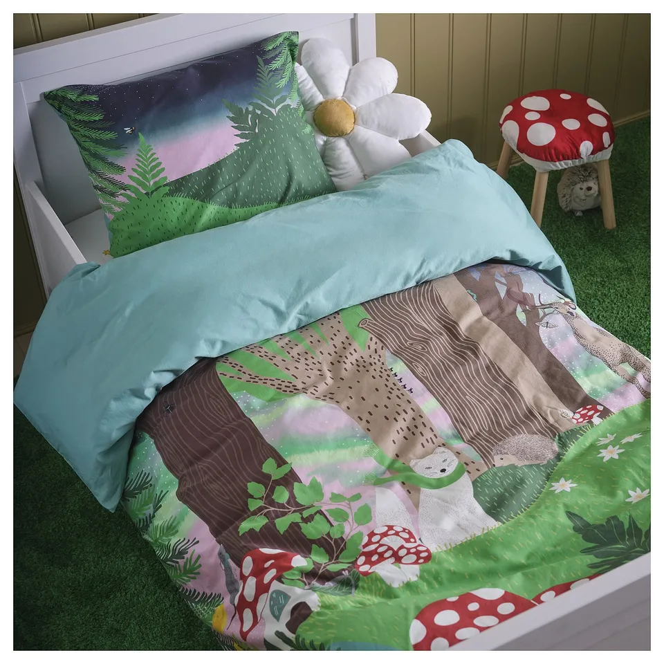 A cosy bed with the SKOGSDUVA star-shaped pillow, featuring a colourful forest design. The pillow is white, large, and soft, perfect for kids rooms.