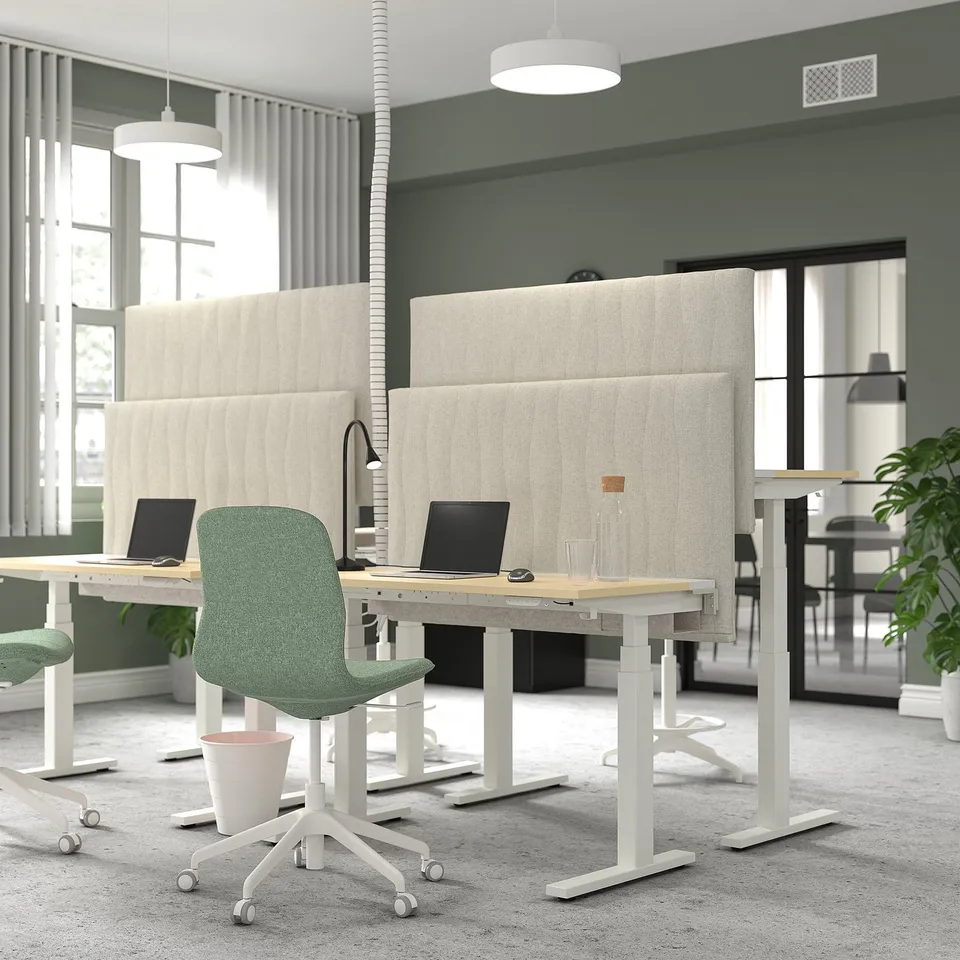 Modern office with MITTZON acoustic screens. Light beige screens on adjustable desks with green chairs. Screens absorb sound, reduce distractions.
