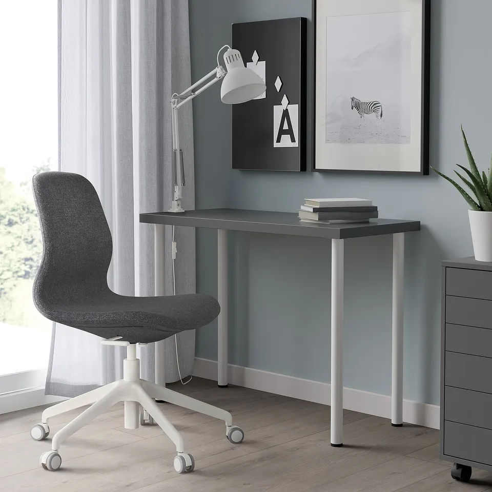 Small grey LINNMON desk against blue wall, paired with black chair, white lamp, and framed art.