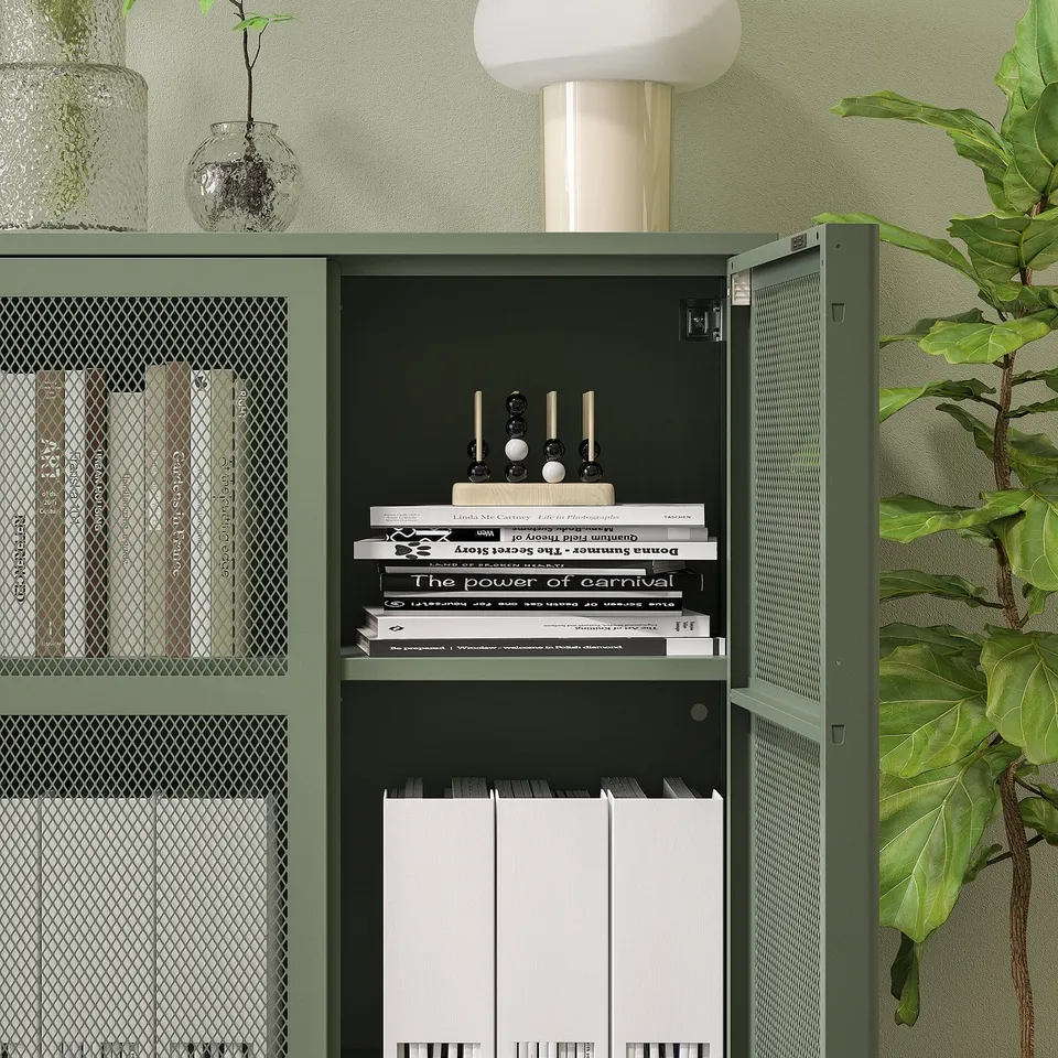 Green IVAR cabinet with mesh door, storing books and folders. A lamp and plant on top.