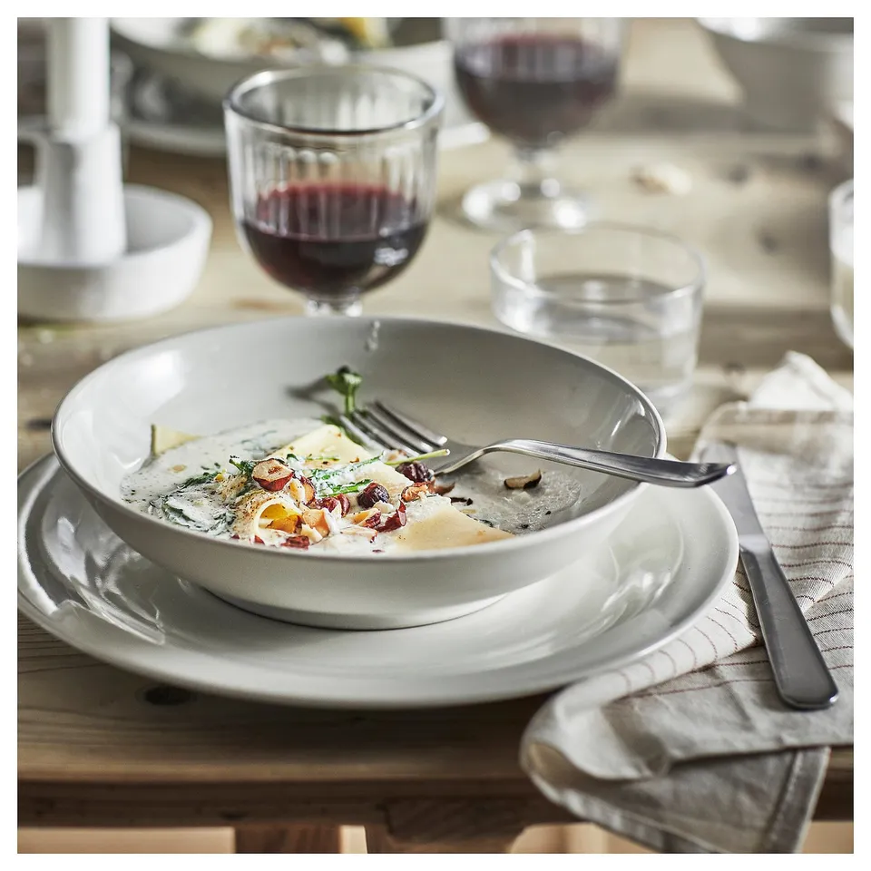 Image a rustic, ceramic dinnerware plate with remaining food and a glass of red wine. A fork rests on the plate, suggesting a meal in progress.