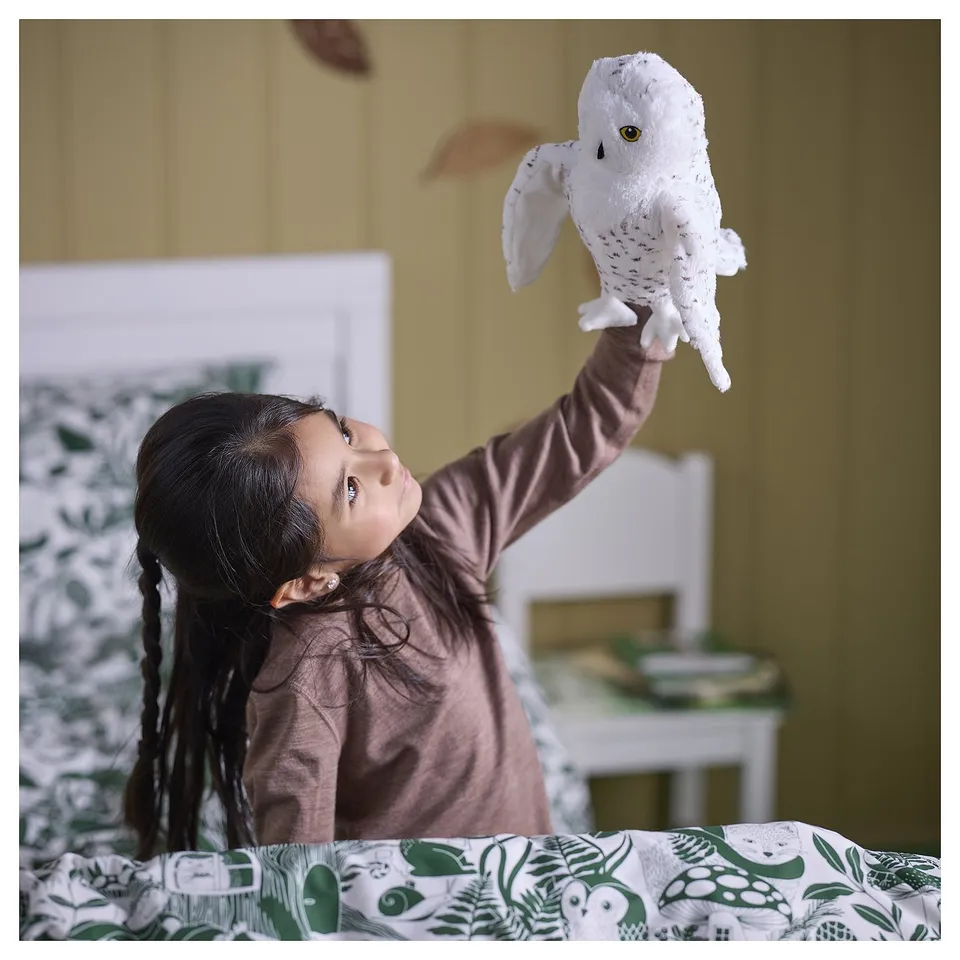 Girl plays with white owl puppet above head.