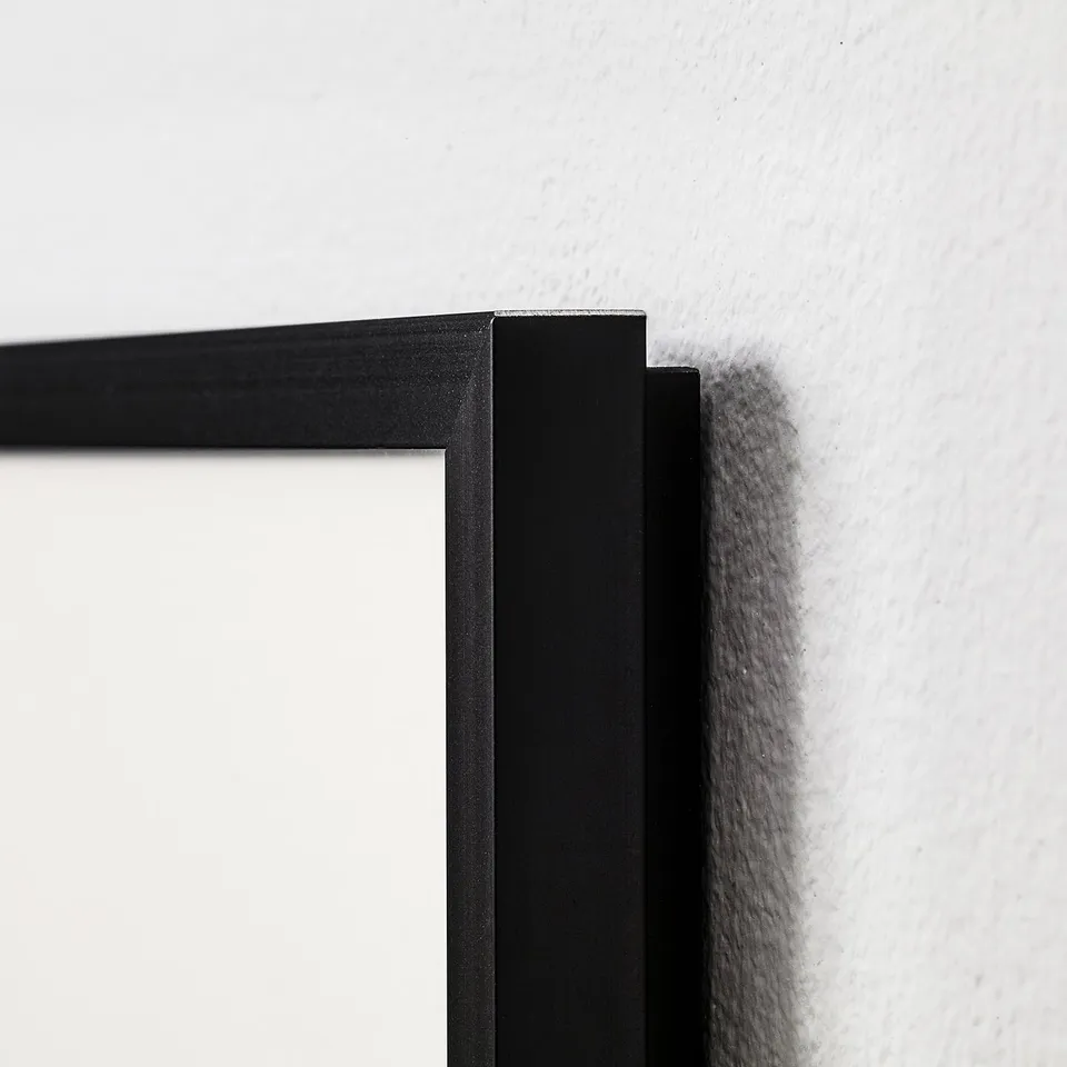 Black photo frame corner, showing high-quality finish and sleek design. Mounted on a white wall.