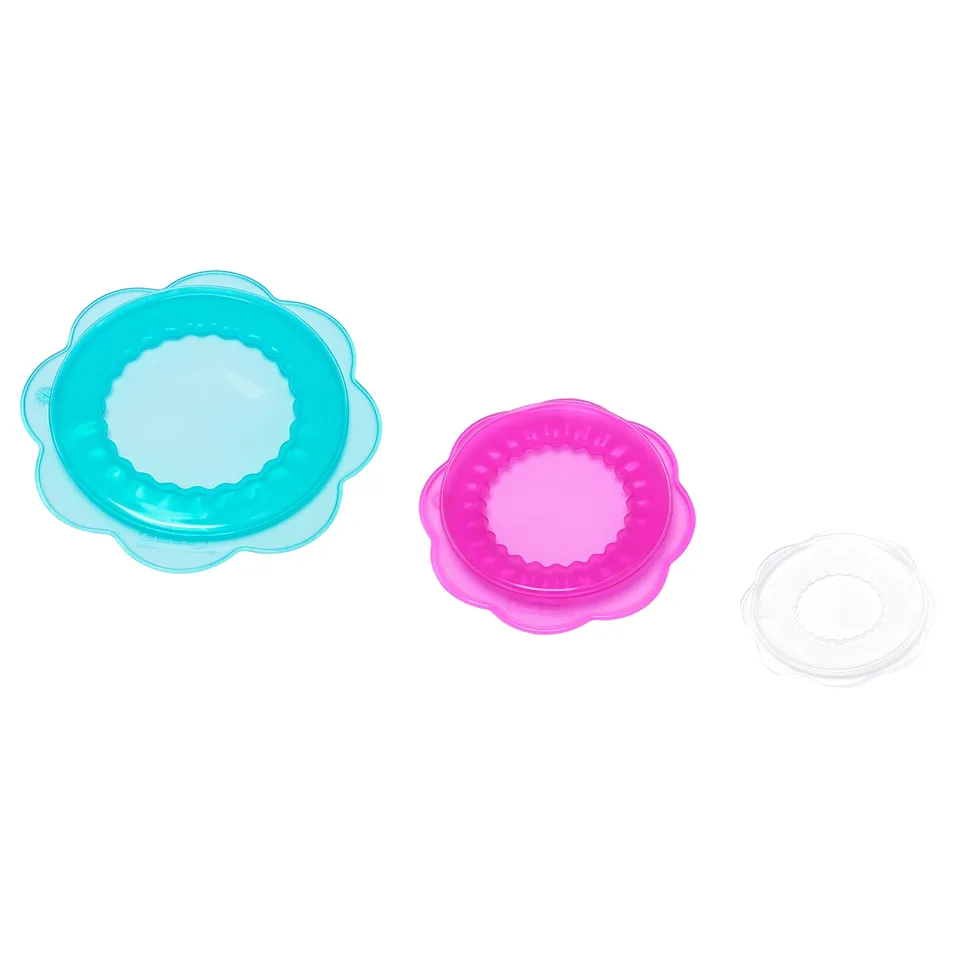 Three coloured flower-shaped silicon covers, blue, pink, and clear, designed to fit and seal various containers, promoting freshness and reusability.