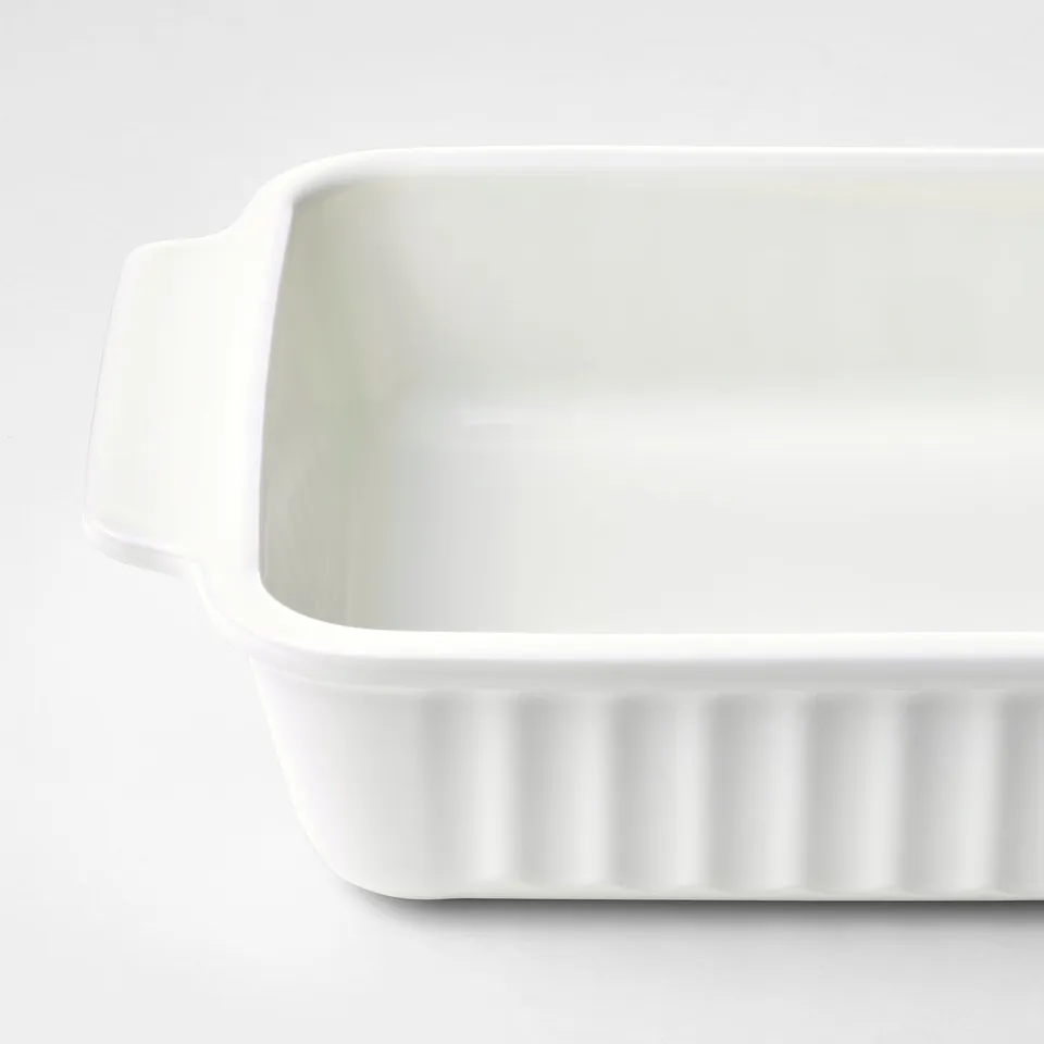 A large, rectangular white baking dish with handles and ribbed base, placed on a white surface.