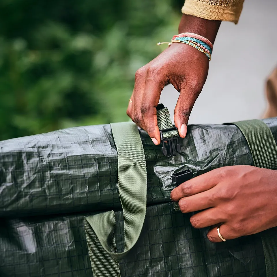Person adjusting sturdy, green-handled shopping bag with durable straps and robust buckles, designed for easy mobility and secure closure.