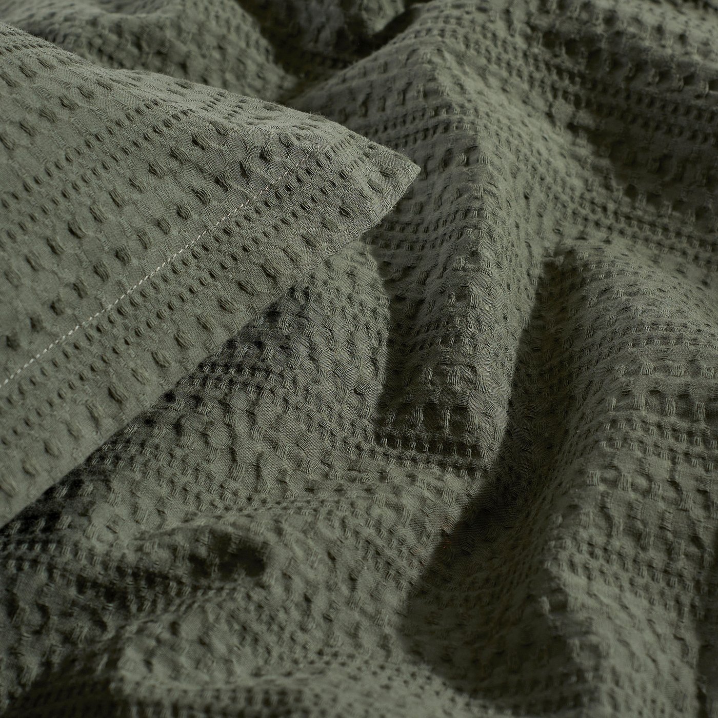 Close-up of soft, green waffle-textured comforter; 100% cotton, detailed weave visible.