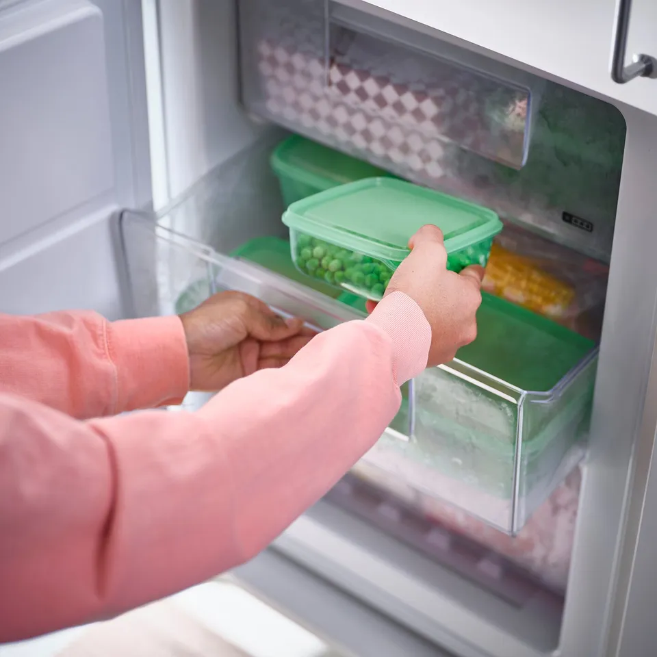 Person opens refrigerator, storing green beans and corn in PRUTA containers.