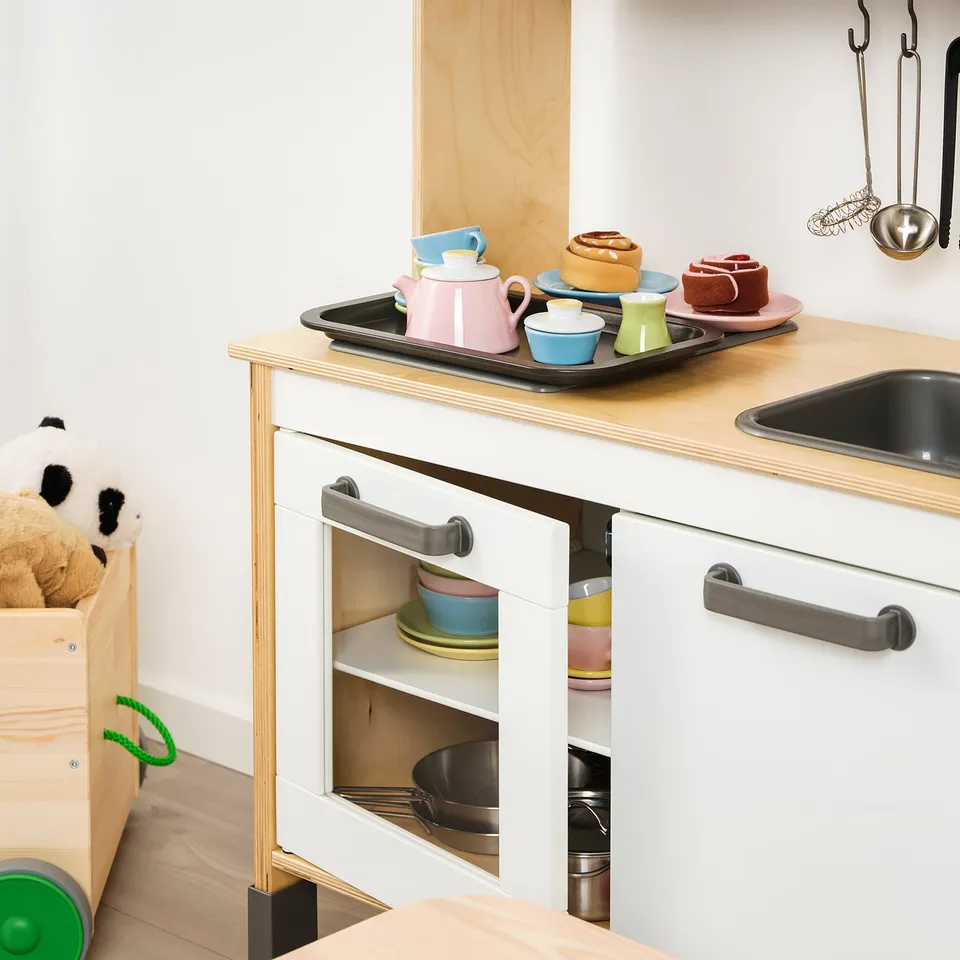 Kids play kitchen with colourful teacups and saucers on tray.