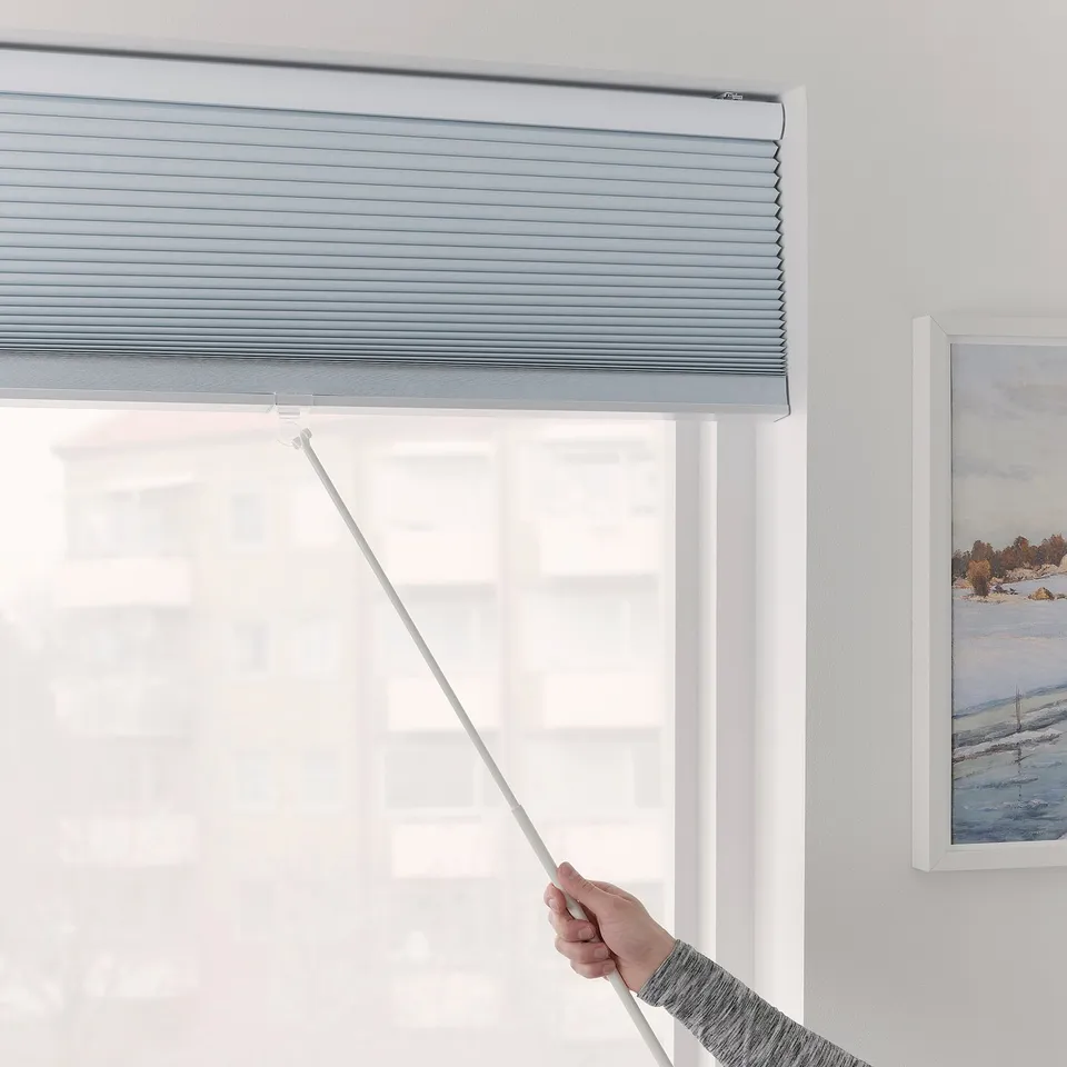 Hand drawing light-blocking blinds down with rod.