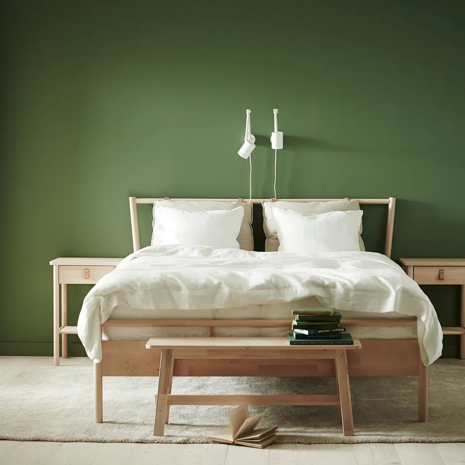 Minimalist bedroom with green walls, white bed, wooden nightstands, and beige STOENSE rug.