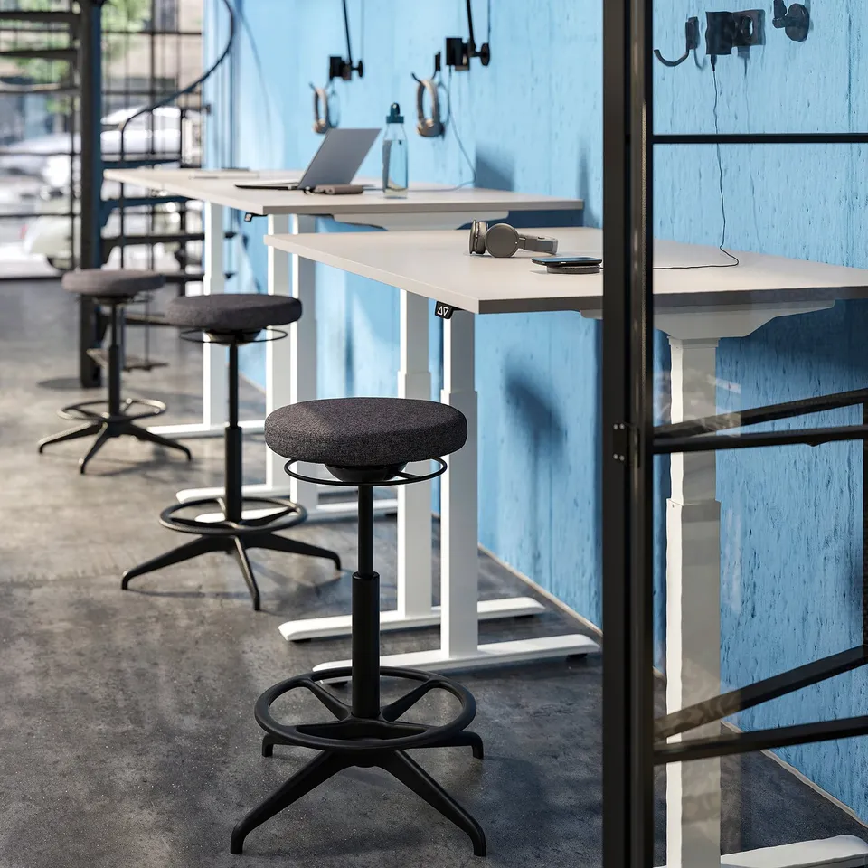 Modern office with blue walls, high stools, and desks with laptops and headphones.