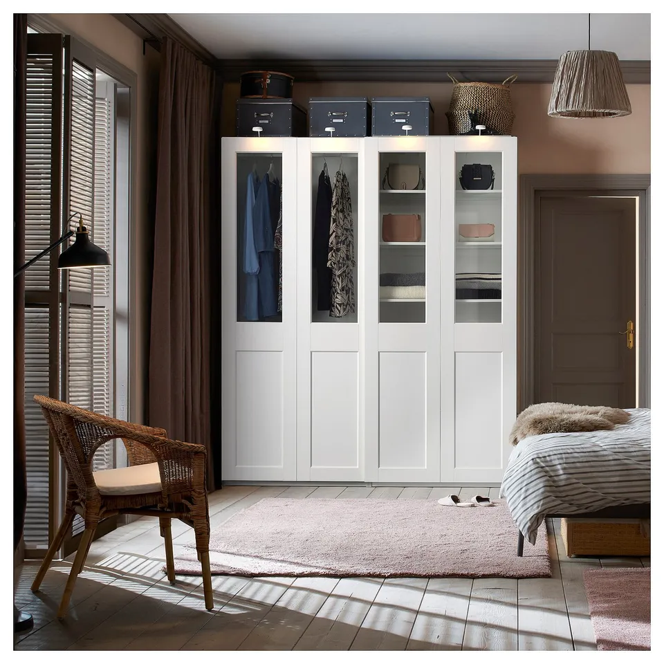 A modern bedroom with a white PAX wardrobe featuring glass doors, storing clothes and accessories.