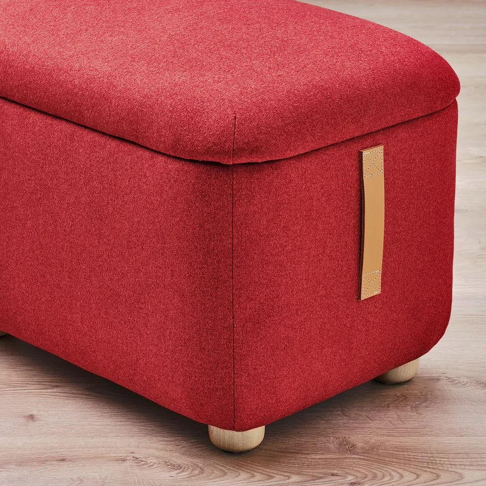 Red fabric-sheathed footstool with storage, wooden legs, and leather handles, offering comfort and style.