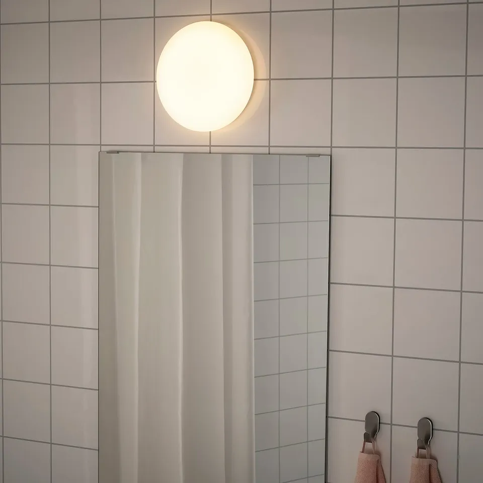 A modern ceiling lamp in a tiled bathroom, emitting a soft, even light. Its wired for indirect lighting and suitable for bathroom use.