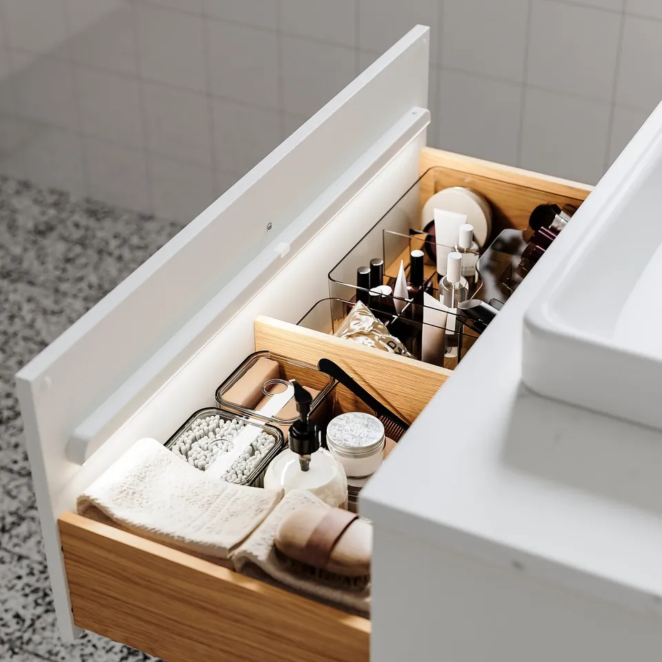 Bathroom drawer with organised toiletries, including bottles, brushes, and a hairdryer, illuminated by automatic led lights.