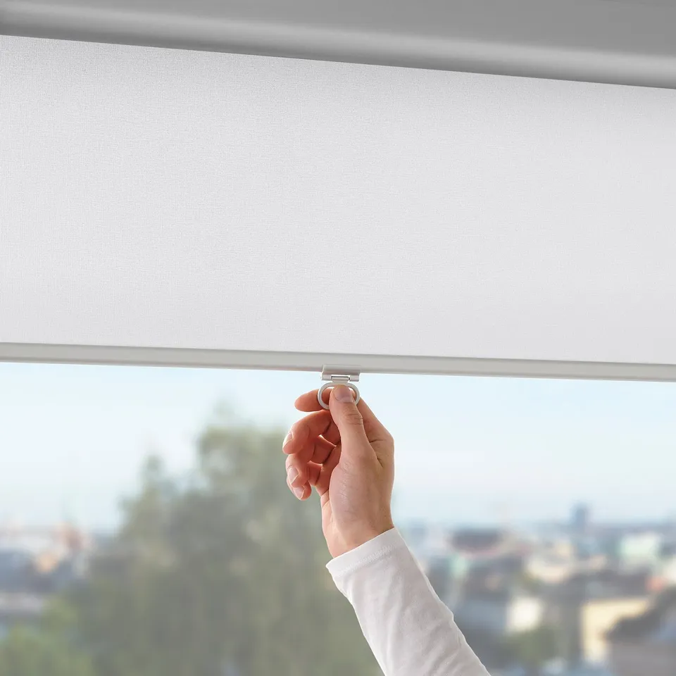 Hand raising cordless roller blind, blocking sunlight; soft-close feature visible.