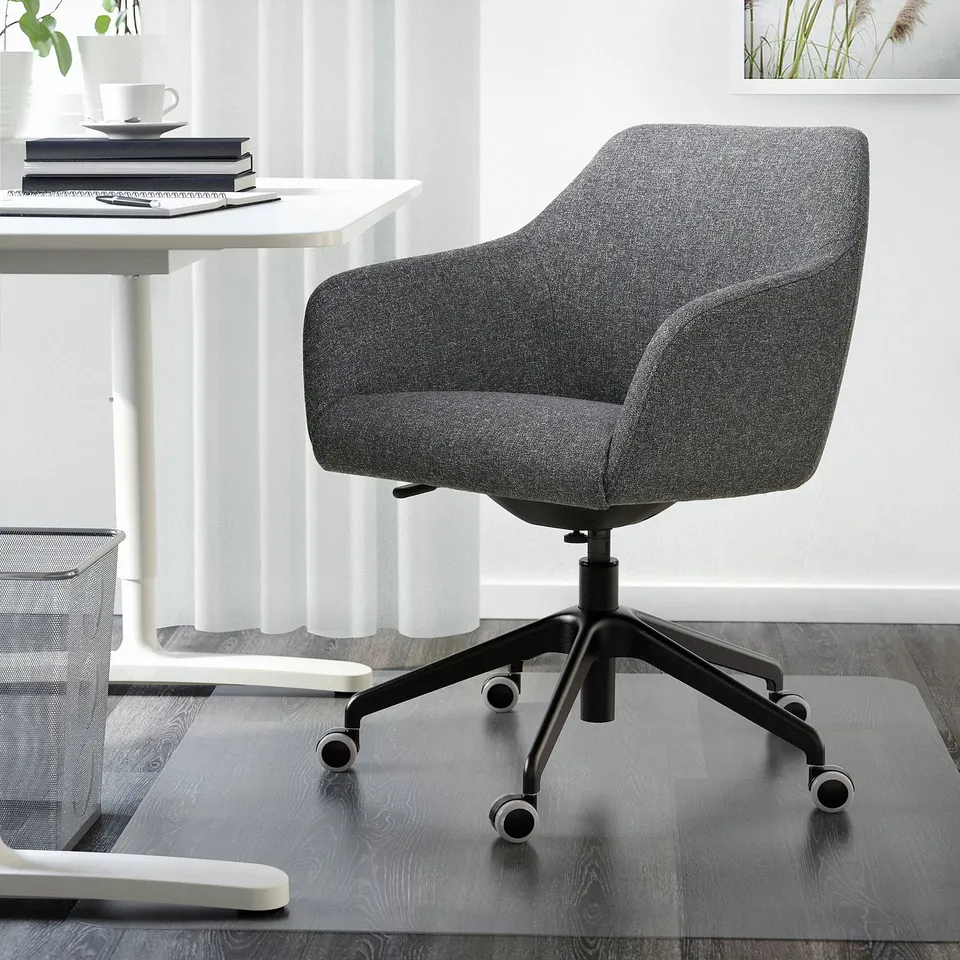 Grey TOSSBERG office chair with cushioned seat and high back, on black casters, under white desk.
