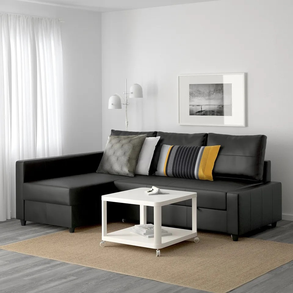Black l-shaped sofa, sleek modern design, cushions, white coffee table, floor lamp, rug, grey walls.