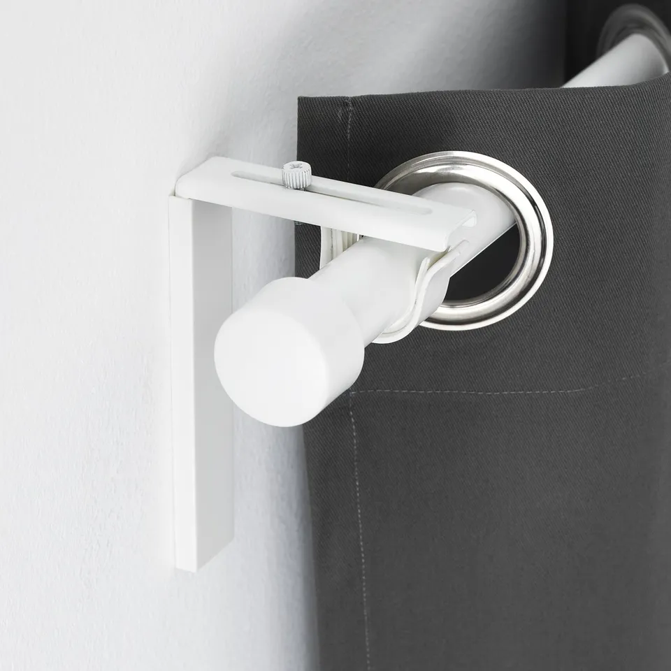 White adjustable curtain rod holder mounted on dark fabric-covered wall, allowing versatile curtain hanging options.