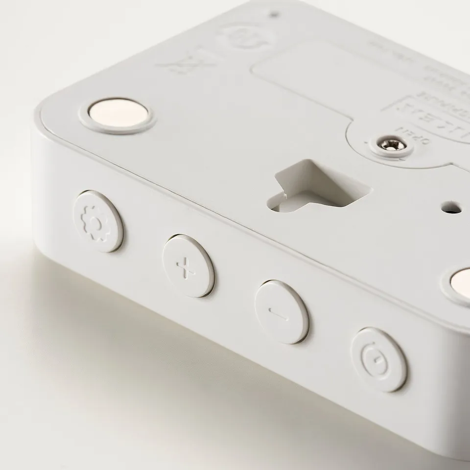 Back of a white digital clock, featuring circular buttons and a magnet for wall attachment.