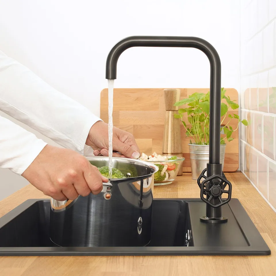 Person washes vegetables in modern kitchen sink with rustic high spout tap, saving water and energy.