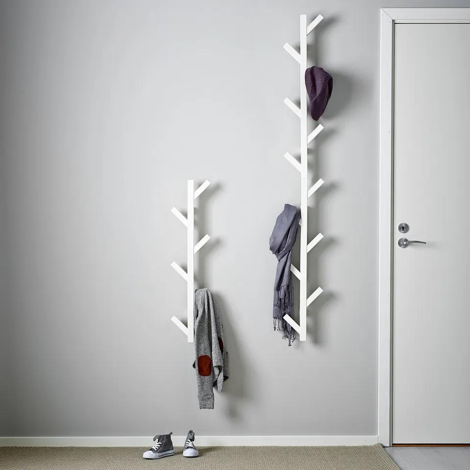 Wall-mount coat rack with two sections, holding jackets, scarves, and a cap, by doorway.