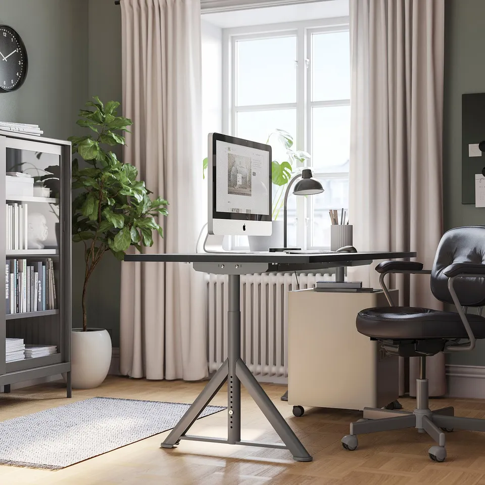 Modern home office with IDÅSEN desk, black chair, and bookshelf. Large window, adjustable desk, cable net, plants, and rug.